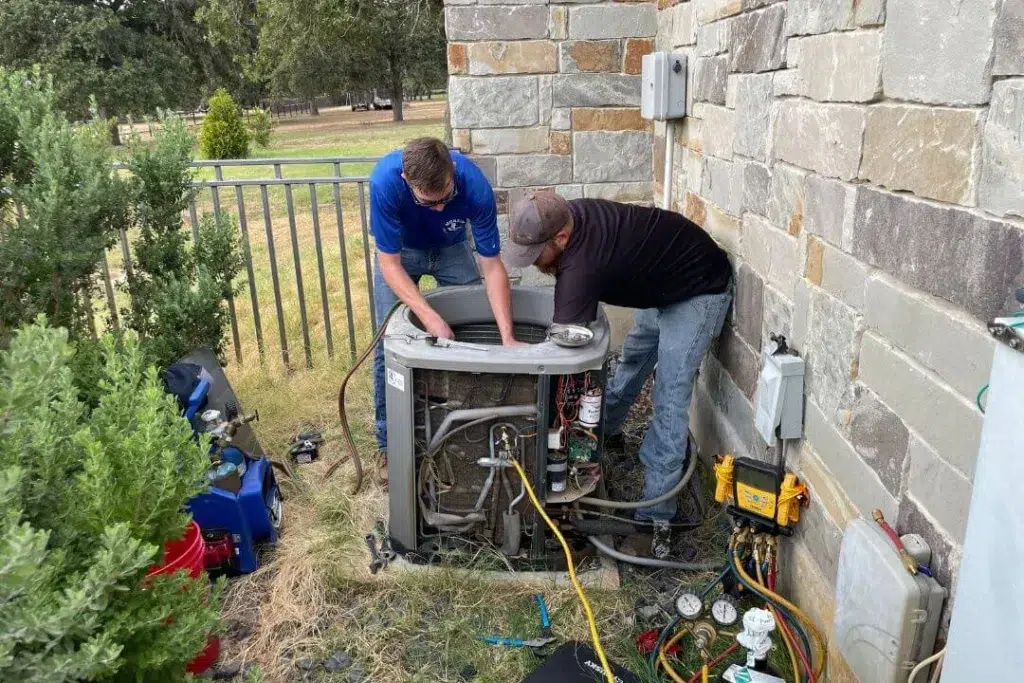 Two technicians repairing an outdoor AC unit.