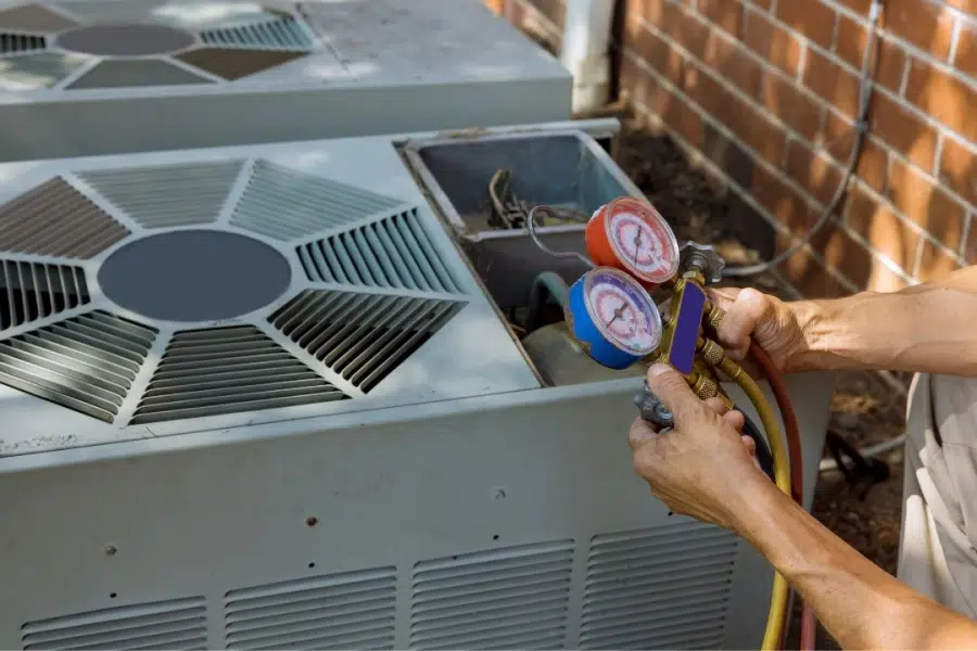 HVAC technician using gauges on air conditioner.