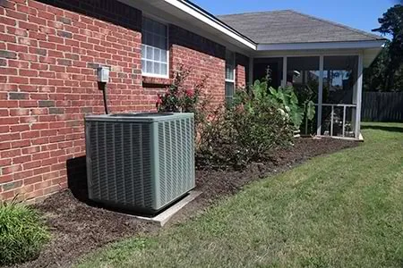 Residential outdoor AC unit beside a brick house with a screened porch