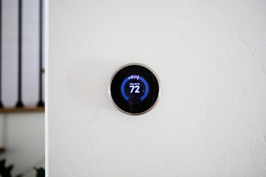 A modern digital thermostat mounted on a white wall, displaying a temperature of 72 degrees Fahrenheit.