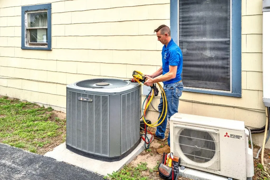 A technician in a blue polo shirt working on an outdoor air conditioning unit