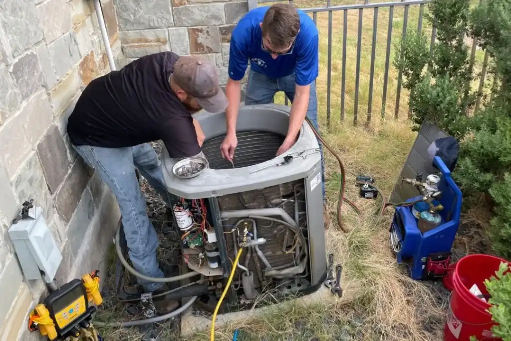 Two technicians are working on an open outdoor air conditioning