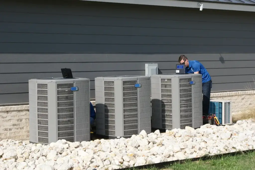 AC Repair technician in a blue polo shirt is working on a set of three large outdoor air conditioning units