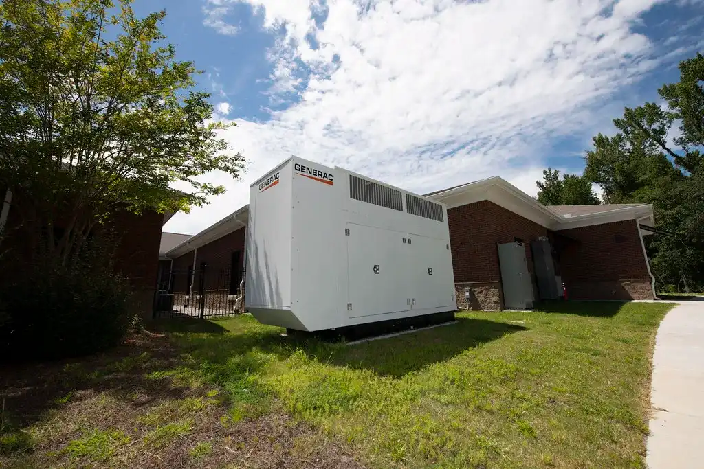 A large white Generac industrial generator installed outside a brick building.