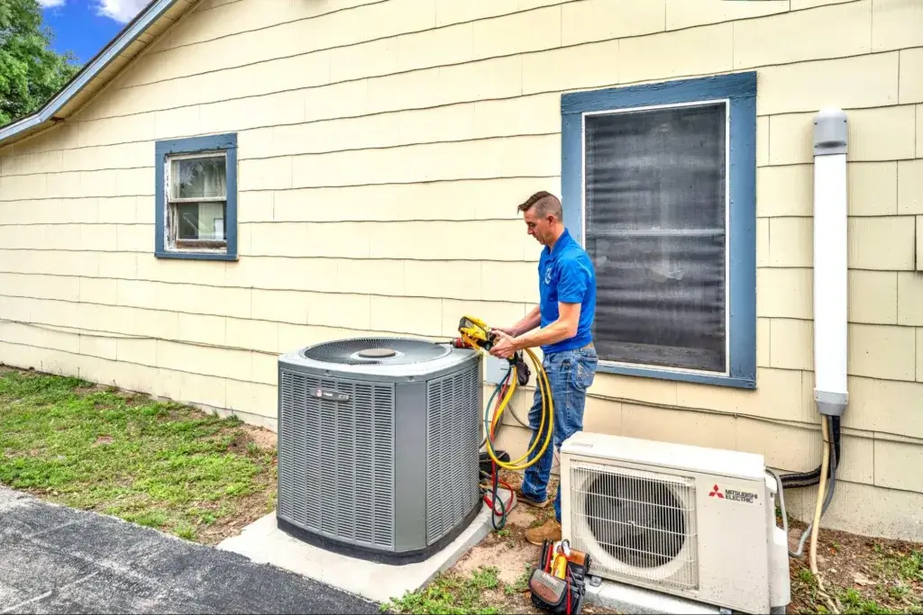 A technician in a blue polo shirt is working on an outdoor air conditioning unit