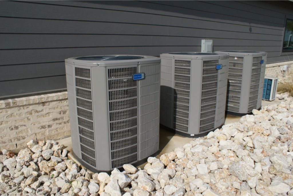 Three large, gray air conditioning units outside a house.