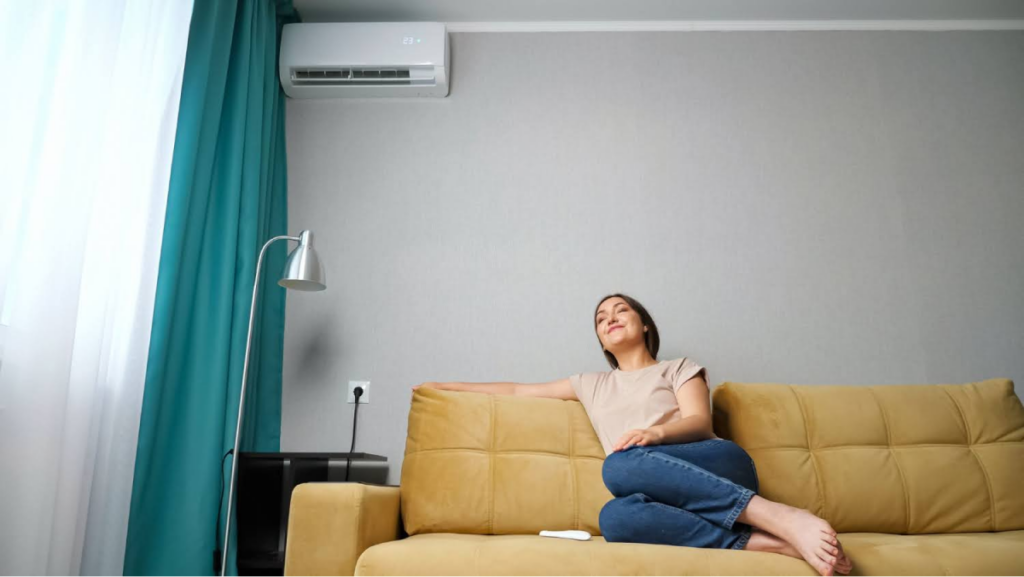 Woman relaxing on a couch in a living room with an air conditioning unit mounted on the wall.