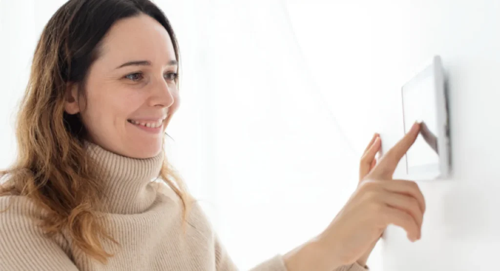 Woman adjusting a digital thermostat on the wall.