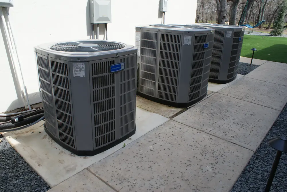 Three large outdoor air conditioning units are installed side by side on concrete pads